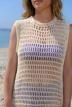 a woman standing on the beach wearing a crochet top and sunglasses with her hands in her pockets