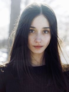 a woman with long black hair and freckles on her face looking at the camera