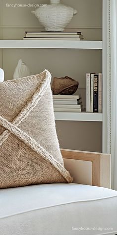 a white couch with a pillow on top of it and bookshelves in the background