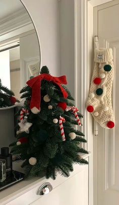 a small christmas tree sitting on top of a mantle next to a mirror with stockings hanging from it