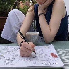 a woman sitting at a table writing on a piece of paper with a cup of coffee in front of her