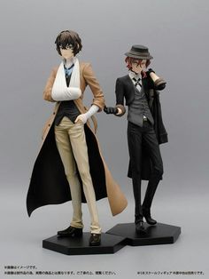 two figurines that are standing next to each other in front of a gray background