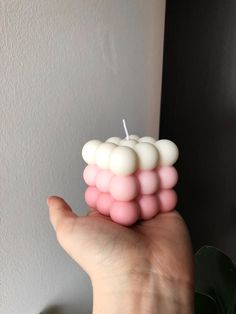 a hand holding a small candle with pink and white candles on it's top