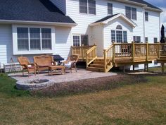 a deck with chairs and fire pit in front of a house