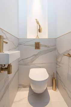 a white toilet sitting in a bathroom next to a sink and gold faucet