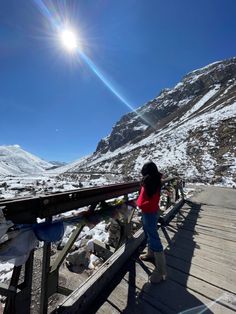 a woman standing on a wooden bridge over snow covered mountains with sun flares in the sky