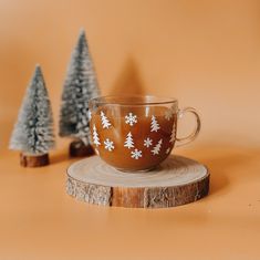 a coffee cup sitting on top of a wooden table next to two small christmas trees