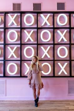 a woman standing in front of a neon wall with xoxo signs on it