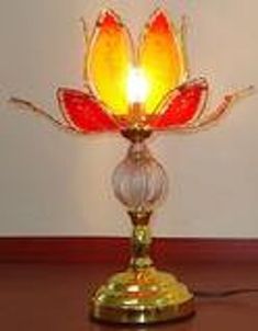 a yellow and red glass candle holder with a light on it's side, sitting on a table