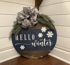 a wooden sign that says hello winter with snowflakes and a bow on it