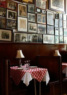 two tables with red and white checkered tablecloths sit in front of a wall full of framed pictures