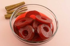 a glass bowl filled with sliced red apples next to cinnamon sticks and an apple cider