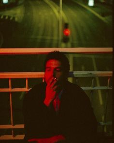 a man sitting on a bench in front of a traffic light at night with his hand to his mouth