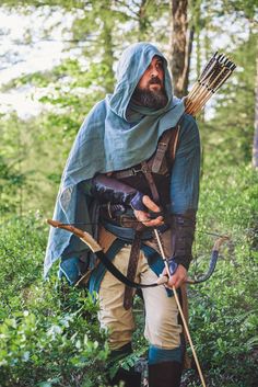 a man dressed in medieval garb holding an arrow and bow while standing in the woods