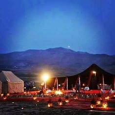 many lit candles are on the ground in front of a tent with mountains in the background