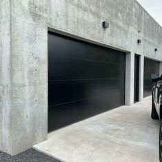 a black car is parked in front of a building with two garage doors on it