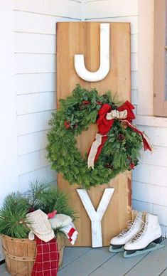 a wooden sign that says joy with wreaths and snow boots in front of it