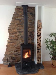 a wood burning stove in a living room next to a stack of firewood and a potted plant