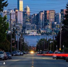 the city skyline is lit up at night with cars parked on the street in front