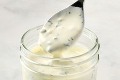 a spoon full of mayonnaise sitting on top of a glass jar filled with dressing