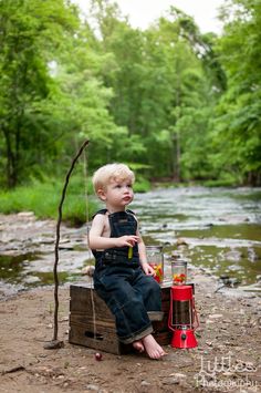 a young boy sitting on top of a wooden crate next to a stream in the woods