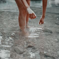 a person is standing in the water with their feet on the ground and one hand reaching for something