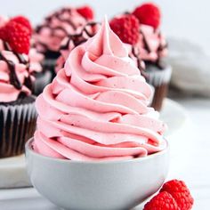 two cupcakes with pink frosting and raspberries on the side, one has a bite taken out