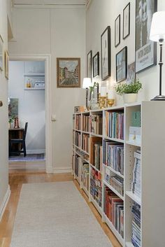 a long hallway with bookshelves and pictures on the wall above it, along with a door leading to another room