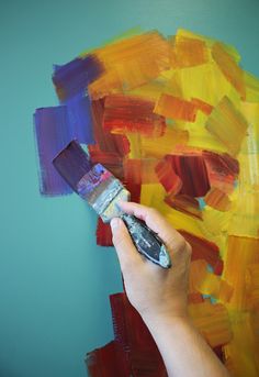 someone is painting the wall with different colors and shapes in their hand, while holding a paintbrush