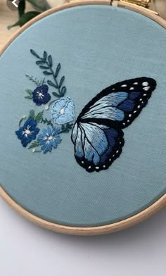 a blue and black butterfly with flowers on it's back is sitting in front of an embroidery hoop