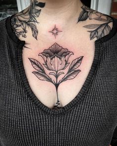 a woman with tattoos on her chest is wearing a black shirt and has a flower tattoo on her chest