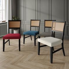 four different colored chairs in a room with wood flooring and gray walls, along with a radiator