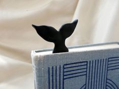 a small book with a whale tail sticking out of it's front cover, sitting on a white sheet