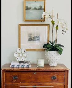 a dresser with flowers and pictures on the wall