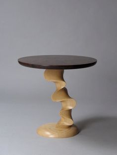 a round wooden table sitting on top of a white floor next to a gray wall