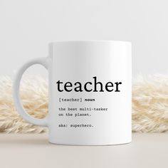 a white coffee mug with the words teacher on it sitting next to a pile of fur