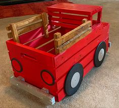 a red wooden toy truck with black wheels on carpeted floor next to rugs