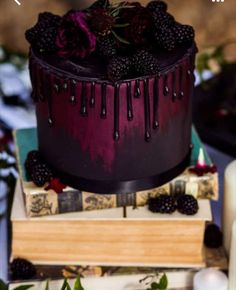 a purple cake with blackberries on top is sitting on some books and has candles in front of it