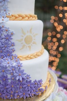 a three tiered cake with purple flowers on the bottom and gold trimmings