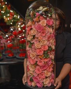 a woman holding a large glass vase filled with pink and orange flowers