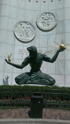 a statue of a man holding a ball in front of a wall with two medallions on it