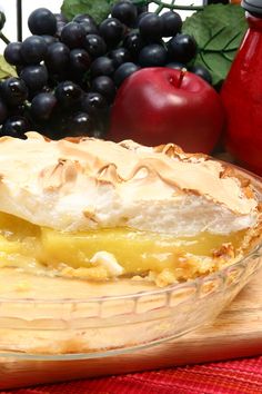 a pie sitting on top of a wooden cutting board next to grapes and an apple