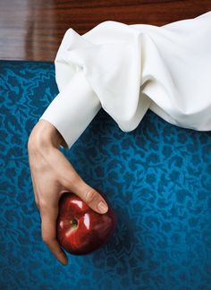 a person holding an apple on top of a blue chair with a white cloth over it