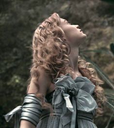 a woman with curly hair is looking up into the sky while wearing gladia garb