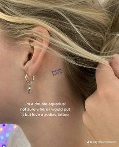 a woman with a small tattoo on her left side of her ear and behind her ear is a pair of earrings