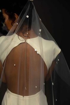 the back of a woman's dress with a veil over her shoulder and pearls on it