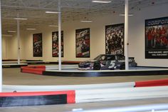 an indoor race track with cars on it and posters hanging from the wall behind them