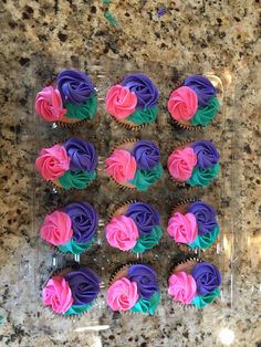 cupcakes with pink, purple and green frosting in a clear plastic container