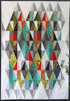 a colorful quilt hanging on the wall in front of a gray wall with a white frame