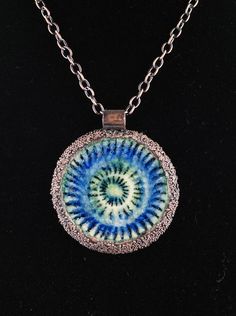 a necklace with a blue and green design on it's center, sitting on a black surface